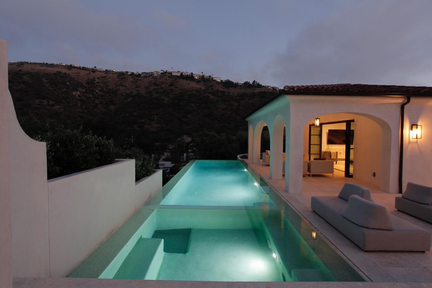 Lit infinity pool at dusk beside an arched pavilion, with the canyon beyond