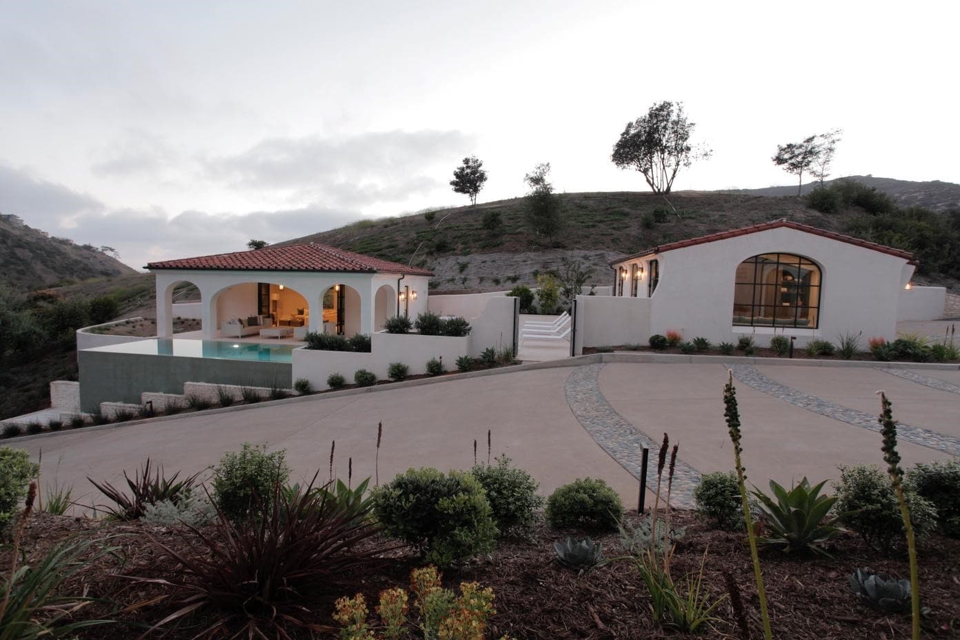 White stucco home and arched pavilion with red tile roofs beside a curved concrete motor court