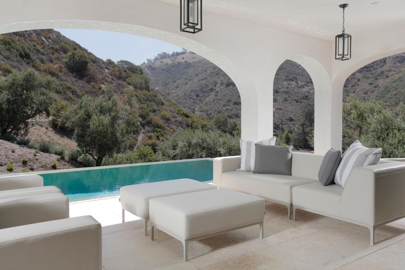 Covered terrace with arched openings and white seating, looking over an infinity pool to the canyon